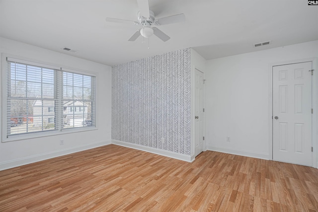 unfurnished room featuring an accent wall, light wood finished floors, visible vents, and baseboards