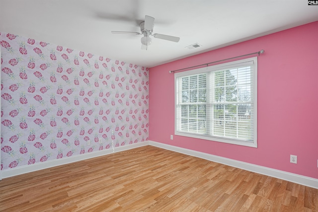 spare room featuring wallpapered walls, baseboards, visible vents, a ceiling fan, and light wood-style flooring