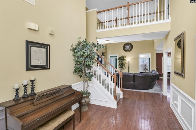 entrance foyer with a wainscoted wall, a decorative wall, stairway, a high ceiling, and hardwood / wood-style floors