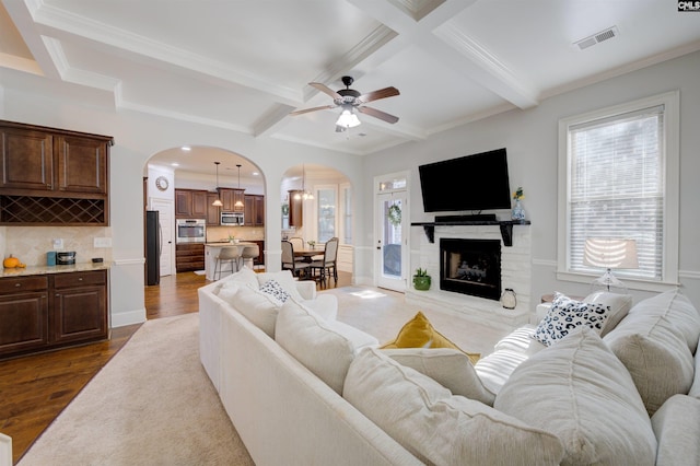 living room featuring dark wood-style floors, visible vents, arched walkways, and beamed ceiling