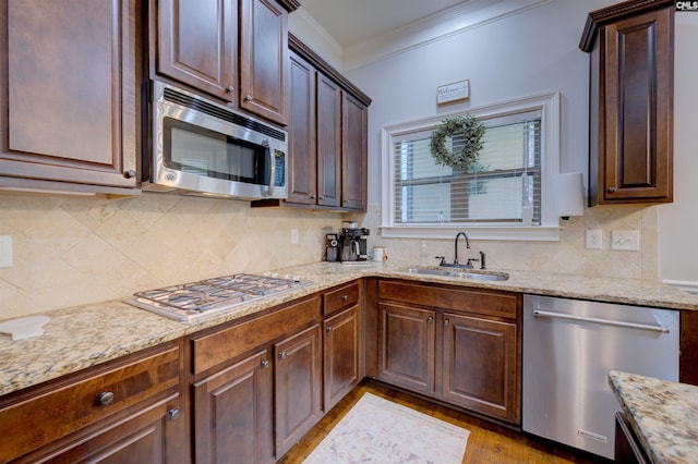 kitchen with appliances with stainless steel finishes, a sink, light stone counters, and ornamental molding