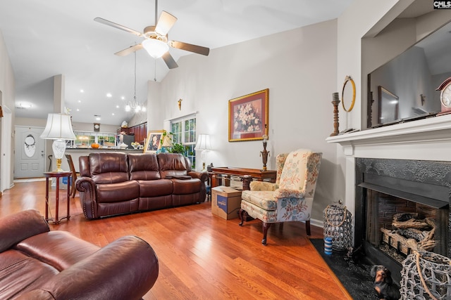 living area featuring light wood finished floors, a fireplace with flush hearth, high vaulted ceiling, and a ceiling fan