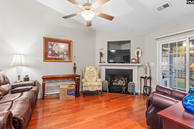 living room featuring lofted ceiling, visible vents, a fireplace with flush hearth, a ceiling fan, and wood finished floors