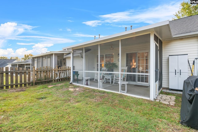 back of property with a shingled roof, a sunroom, fence, and a lawn