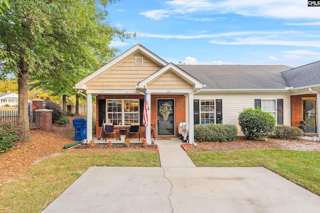 view of front facade featuring covered porch, a front yard, fence, and brick siding