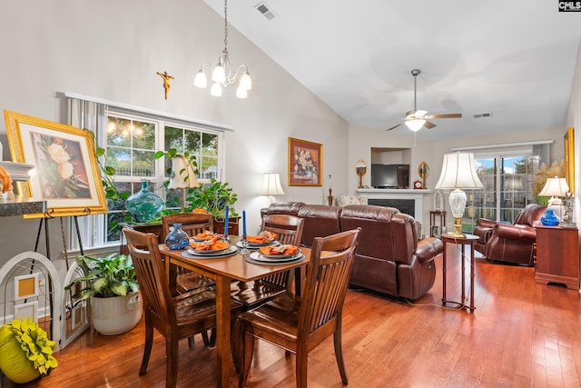 dining area featuring light wood-type flooring, visible vents, a fireplace, and ceiling fan with notable chandelier