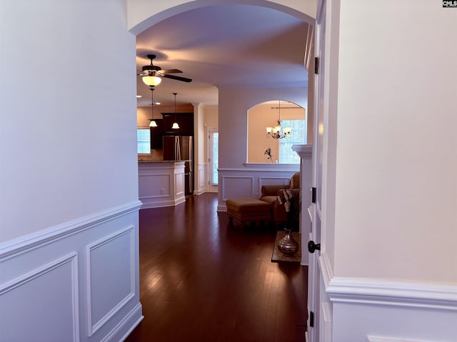 hallway featuring arched walkways, dark wood-style flooring, and a decorative wall