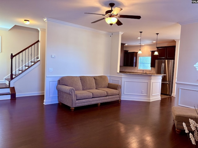 living room with a ceiling fan, stairway, ornamental molding, dark wood-style flooring, and a decorative wall