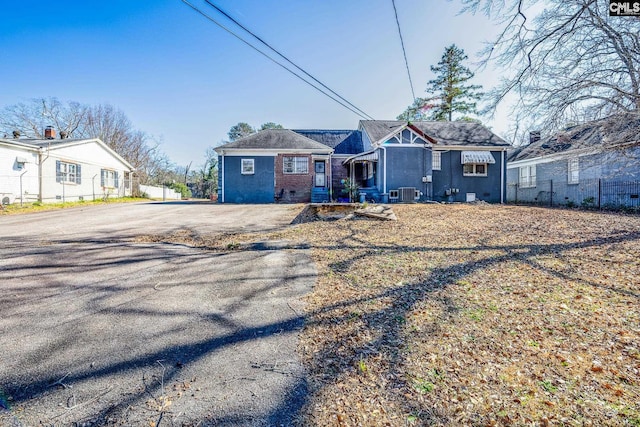 view of front of property featuring aphalt driveway, central AC unit, brick siding, and fence