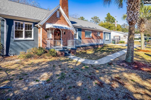 tudor home featuring brick siding, a chimney, and a shingled roof