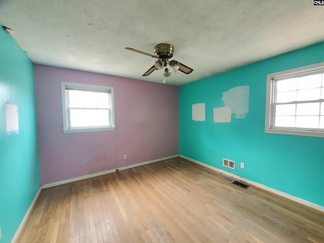 empty room featuring a textured ceiling, visible vents, and wood finished floors