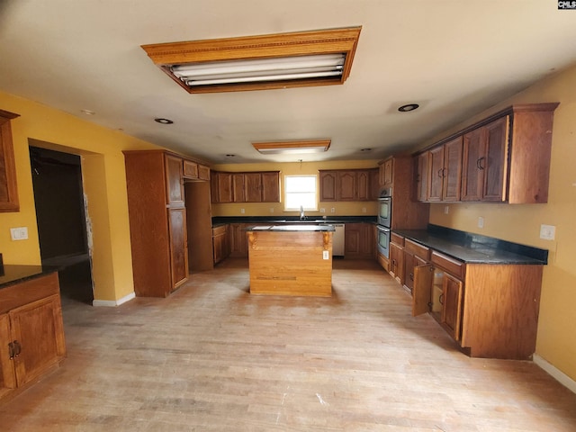 kitchen with double oven, light wood-style flooring, a kitchen island, baseboards, and dark countertops