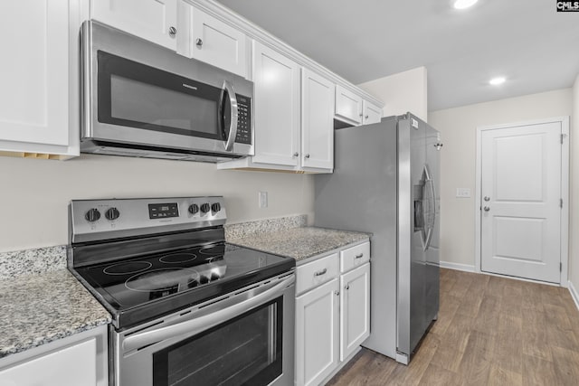 kitchen featuring light stone countertops, white cabinetry, stainless steel appliances, and wood finished floors