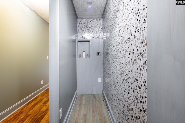 corridor with a textured ceiling, baseboards, and wood finished floors