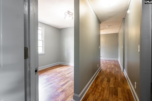 corridor featuring a textured ceiling, baseboards, and wood finished floors