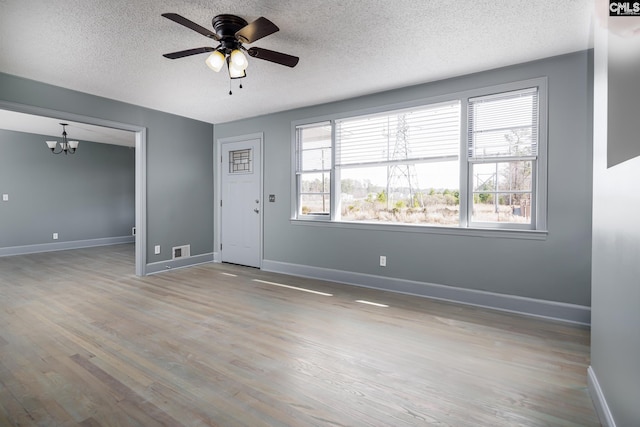 interior space featuring baseboards, visible vents, wood finished floors, a textured ceiling, and ceiling fan with notable chandelier