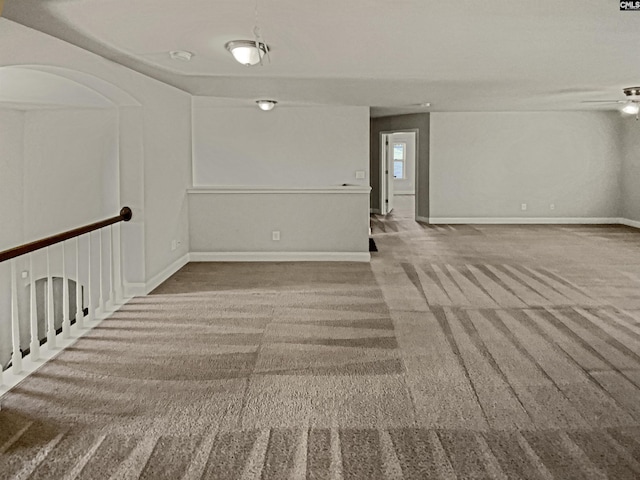 unfurnished room featuring arched walkways, carpet flooring, a ceiling fan, and baseboards