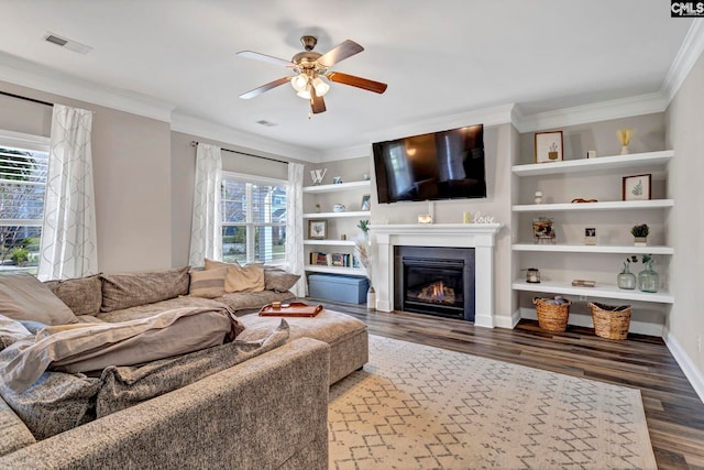 living room with visible vents, a glass covered fireplace, crown molding, and wood finished floors