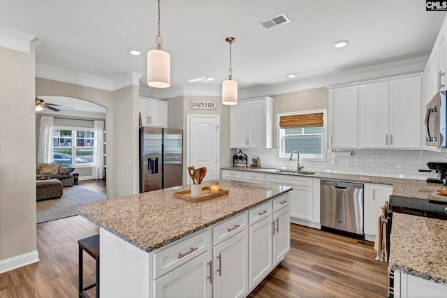 kitchen featuring visible vents, arched walkways, appliances with stainless steel finishes, a center island, and a sink