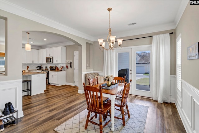 dining room featuring arched walkways, a wainscoted wall, dark wood finished floors, visible vents, and ornamental molding