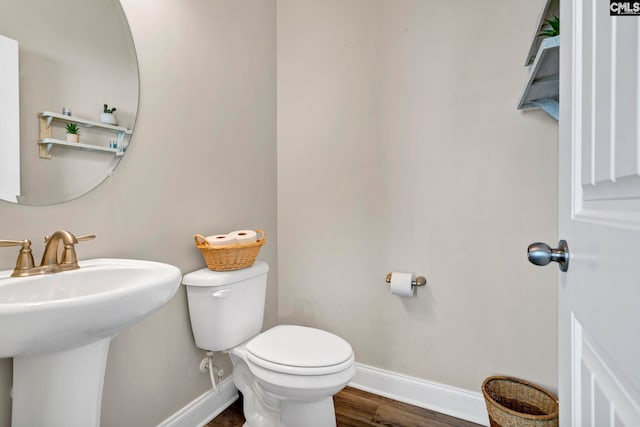 half bath with a sink, wood finished floors, toilet, and baseboards