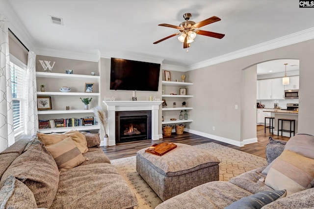 living area featuring arched walkways, light wood-style flooring, visible vents, baseboards, and a glass covered fireplace