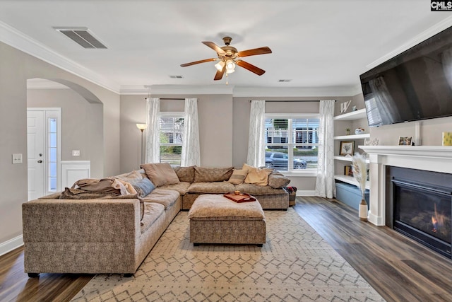 living area with arched walkways, wood finished floors, visible vents, a glass covered fireplace, and crown molding