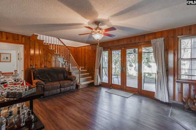 living area with ceiling fan, wood walls, wood finished floors, stairs, and french doors