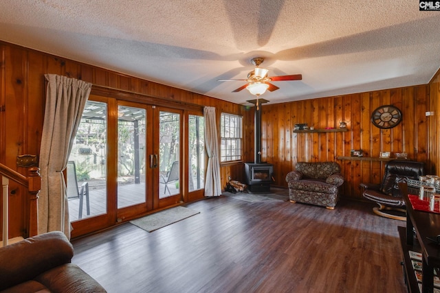 interior space with wood walls, wood finished floors, a ceiling fan, french doors, and a wood stove