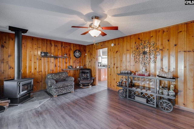 sitting room with a ceiling fan, a wood stove, a textured ceiling, and wood finished floors