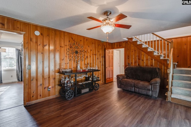 living room with wooden walls, baseboards, a ceiling fan, stairway, and wood finished floors