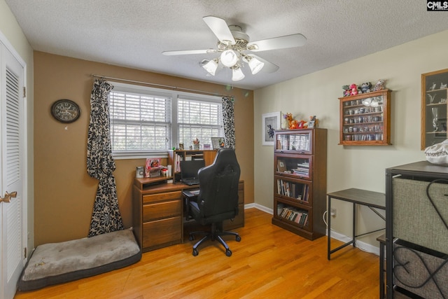 office area with light wood-type flooring, ceiling fan, a textured ceiling, and baseboards