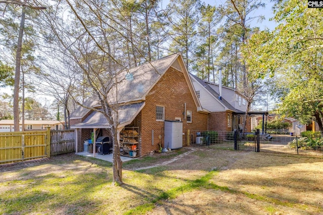 rear view of house with central AC, brick siding, a lawn, and a gate