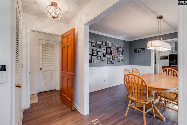 dining area with a wainscoted wall, a textured ceiling, ornamental molding, and wood finished floors