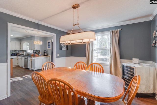 dining room with a wainscoted wall, dark wood-style flooring, a textured ceiling, and crown molding