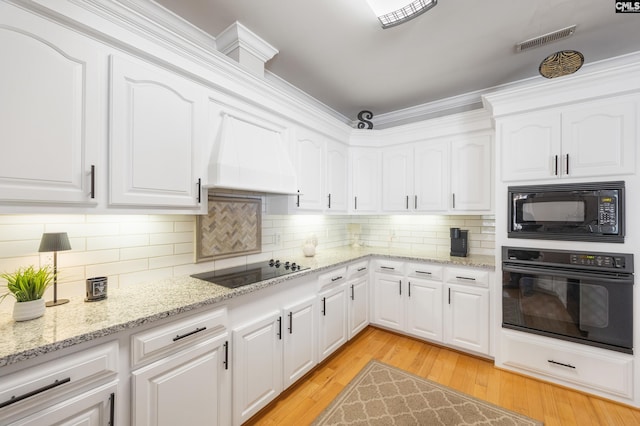 kitchen with visible vents, light wood-style floors, white cabinets, premium range hood, and black appliances