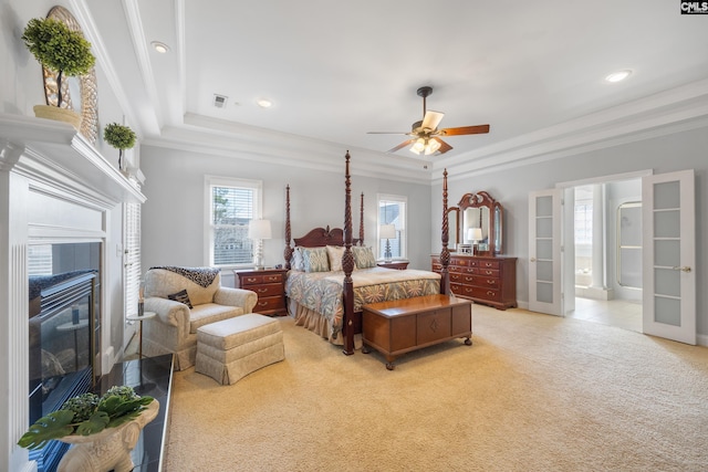 bedroom with a tile fireplace, light carpet, french doors, ornamental molding, and a raised ceiling