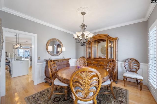 dining area featuring light wood-type flooring, a chandelier, crown molding, and wainscoting