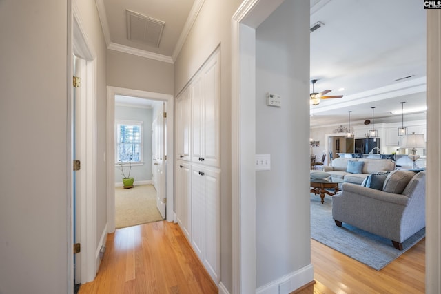 hall featuring baseboards, ornamental molding, visible vents, and light wood-style floors