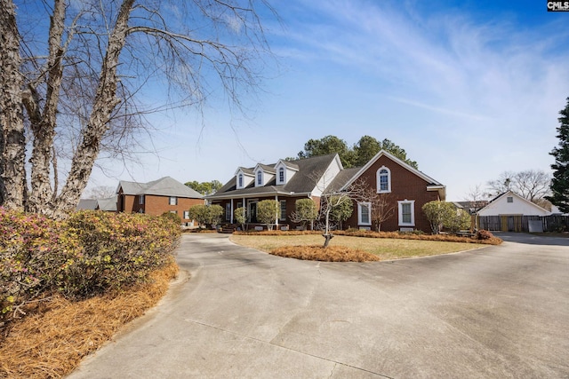 cape cod house with driveway, brick siding, and fence