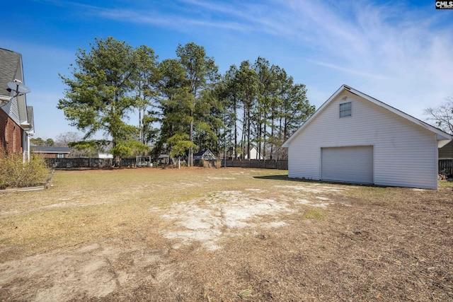 view of yard with dirt driveway, fence, a detached garage, and an outdoor structure