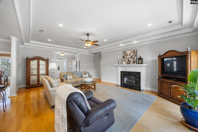 living room with light wood-style floors, a tray ceiling, crown molding, and a tile fireplace