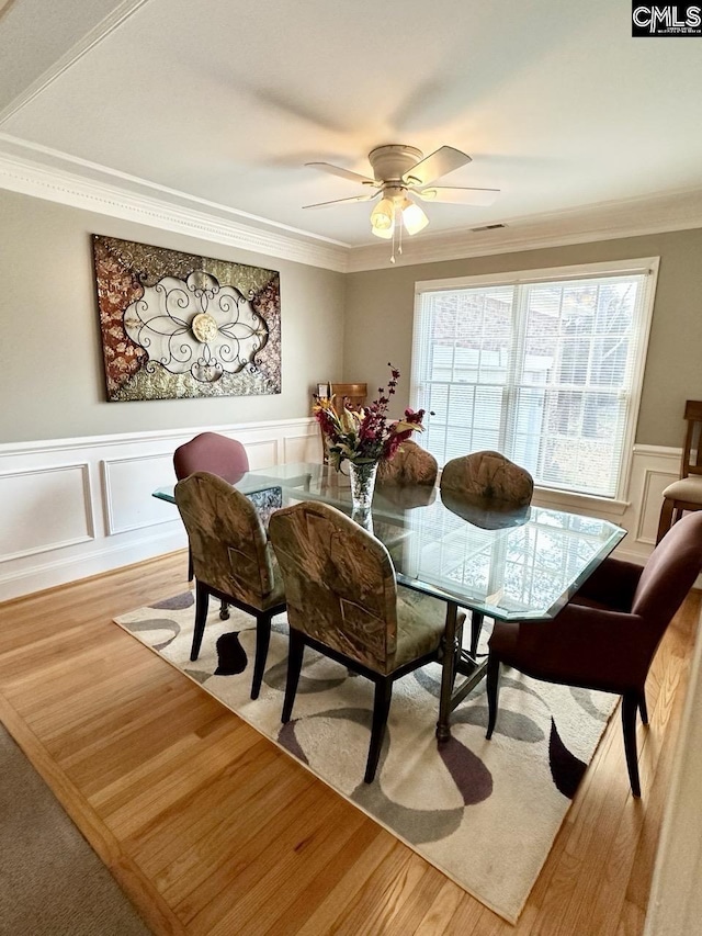 dining space with ornamental molding, a wainscoted wall, and light wood finished floors