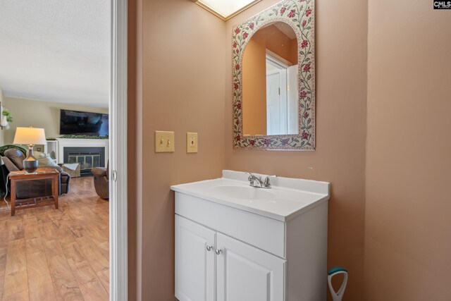 bathroom with a glass covered fireplace, wood finished floors, and vanity