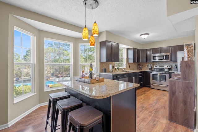 kitchen featuring light stone counters, light wood finished floors, stainless steel appliances, tasteful backsplash, and dark brown cabinetry
