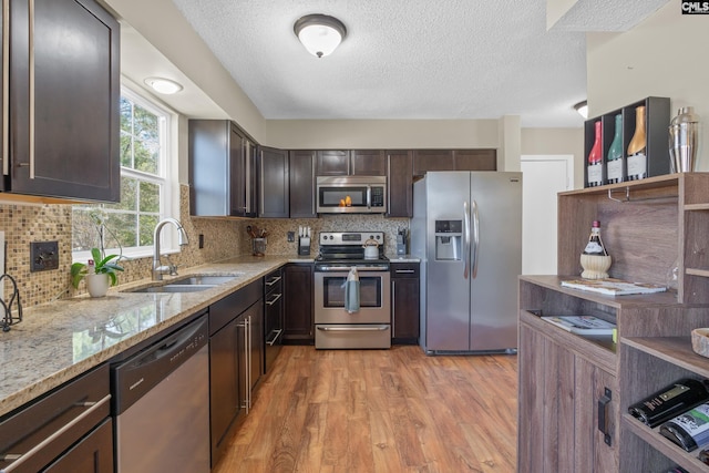 kitchen with light stone counters, stainless steel appliances, a sink, dark brown cabinets, and light wood-type flooring