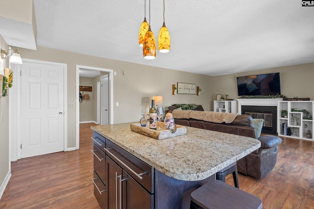 kitchen featuring dark wood-type flooring, a glass covered fireplace, pendant lighting, and baseboards
