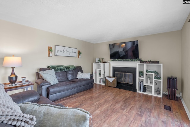 living room featuring baseboards, visible vents, a fireplace with flush hearth, radiator heating unit, and wood finished floors