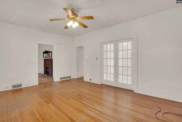 empty room featuring french doors, a fireplace, light wood-style flooring, and visible vents