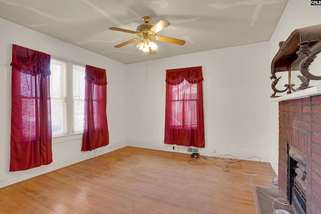 unfurnished living room with baseboards, visible vents, a ceiling fan, wood finished floors, and a fireplace